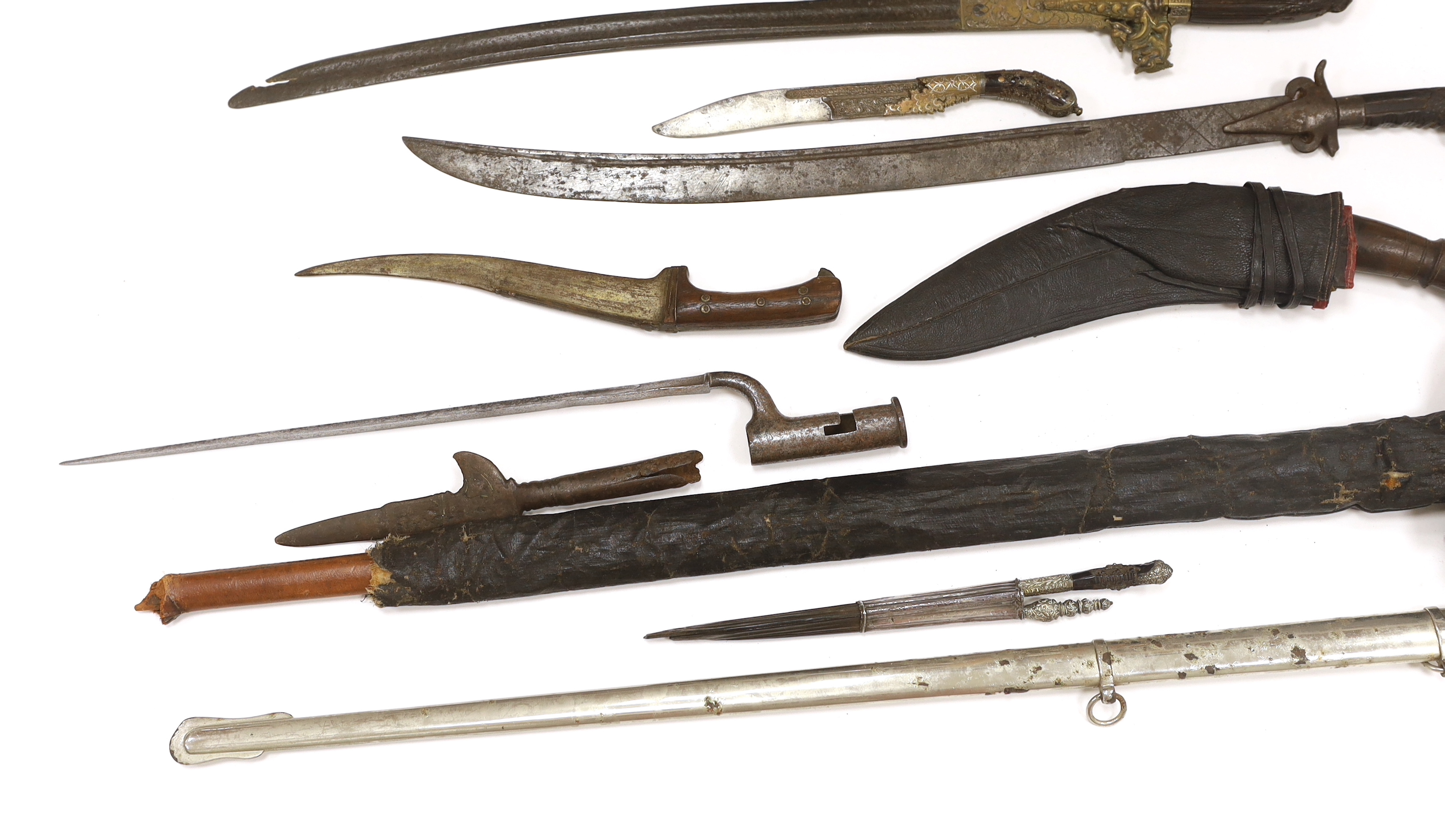 Two Sinhalese daggers and a kukri, a silver inlaid Kirichchiya dagger, together with another in a scabbard with a long pin, another dagger with a wooden handle, a head of a brass inlaid iron pole arm, a George V 1897 pat